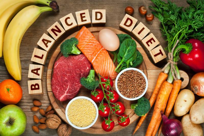 Healthy food kept on a wooden table with wooden blocks showing the word balanced diet kept inbetween them.