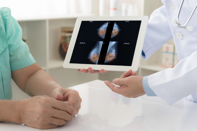 A doctor explains the mammogram results displayed on a digital tab to a patient sitting in front of him.