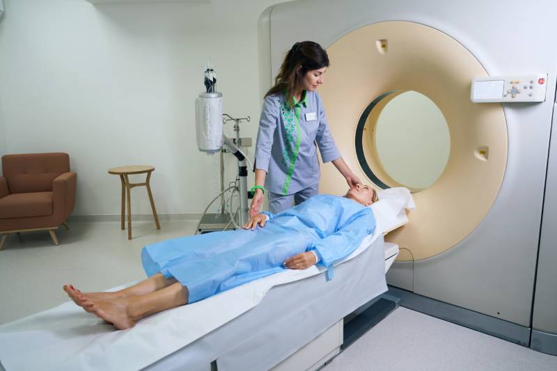Image of a technologis preparing an adult woman lying on a sliding table for a CT scan.