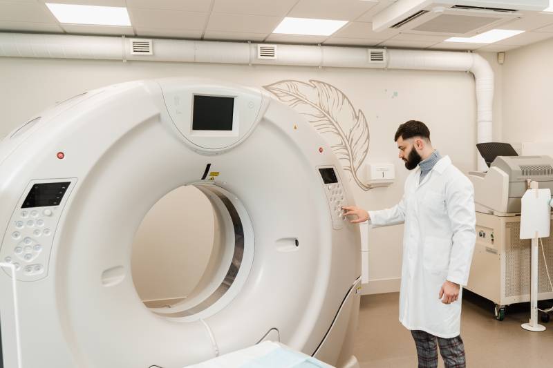 A male radiologist setting the CT scanner inside an imaging room.