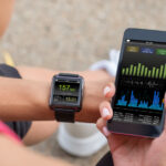 A female runner sitting down after a workout looking at her mobile fitness app and smart watch heart rate monitor.