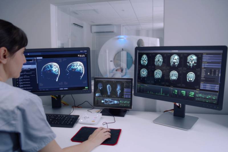 Rear view of a female radiologist sitting in a control room watches at monitors with displayed brain scans results.
