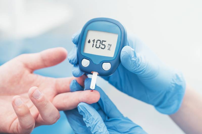 Hands of a lab technician taking blood samples from a patient's finger using a glucometer.