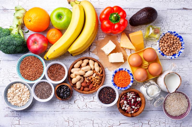 Fruits, vegetables, dairy products, eggs, seeds, healthy fats and grains arranged on a wooden table depicting a Ovo-lacto vegetarian diet concept.