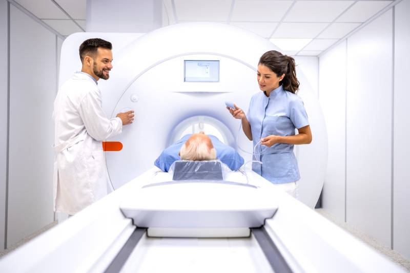 A male radiologist and female technician preparing a patient lying on the sliding table for an MRI procedure.