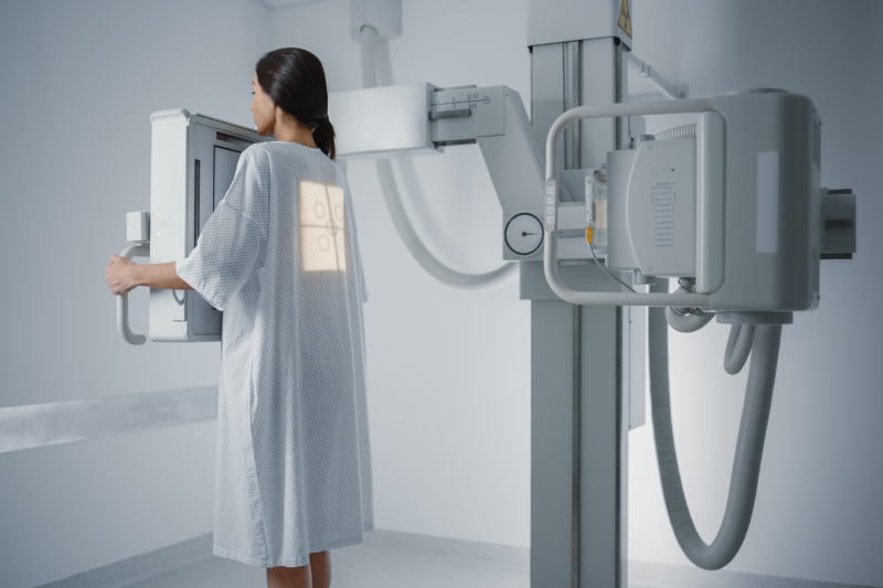 A woman in a medical gown standing in front of the x ray machine in a radiology room.