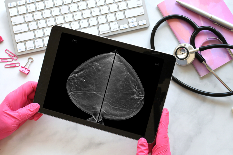 A radiologist wearing pink gloves examines mammogram scan results displayed on a tablet to detect signs of breast cancer.