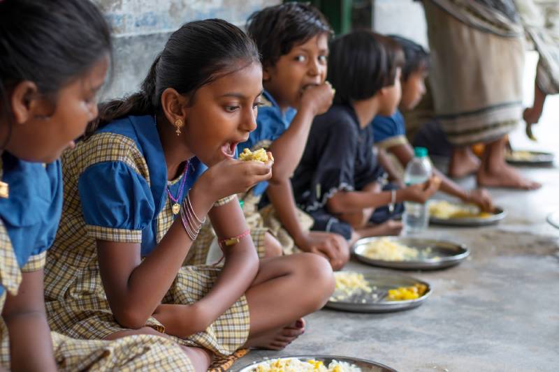 Image of students sitting on the floor having mid day meal at school.