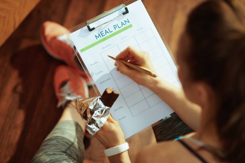 A healthy and fit woman in sport clothes with chocolate raw protein bar in one hand filling her meal plan.