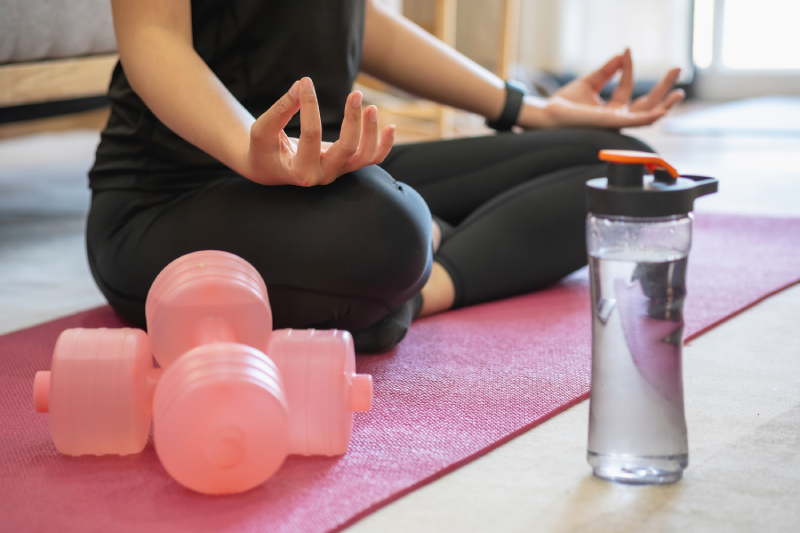 A young woman sitting on a yoga mat doing breathing exercises or meditation at home.