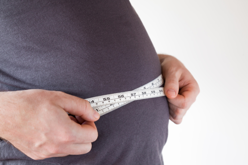 Close up image of a fat and overweight man measuring his waist using a measuring tape.