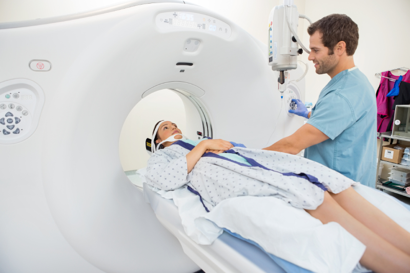 A male radiographer preparing a female patient lying on the CT scan table for a scan.
