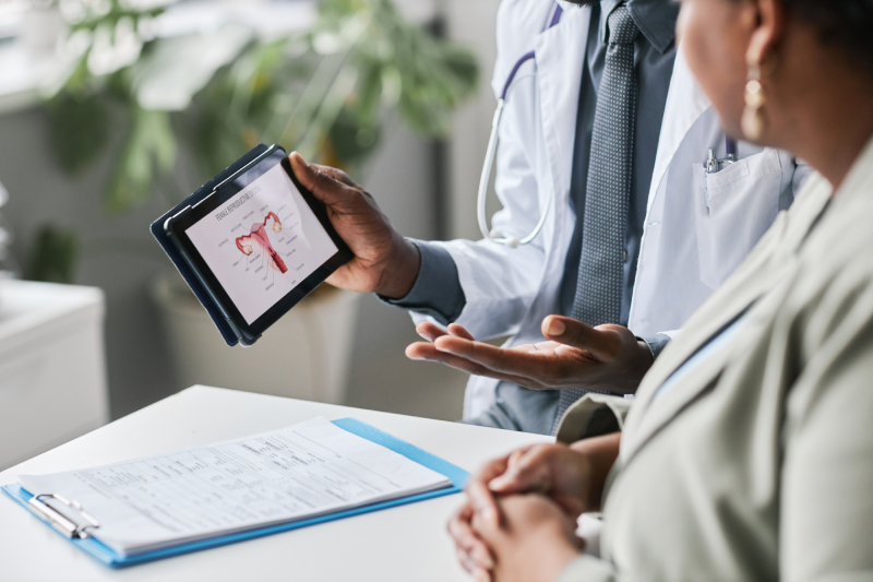 A male and a female doctor discussing holding a tablet displaying the image of uterus and a writing pad with notes kept on the table infront of them.