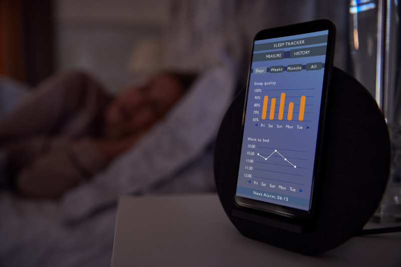 Blurred image of a woman sleeping on her bed at the backgroundwith sleep tracker running on the mobile phone on her bedside.