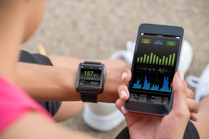 A female athlete looking at her mobile and smart watch heart rate monitor.