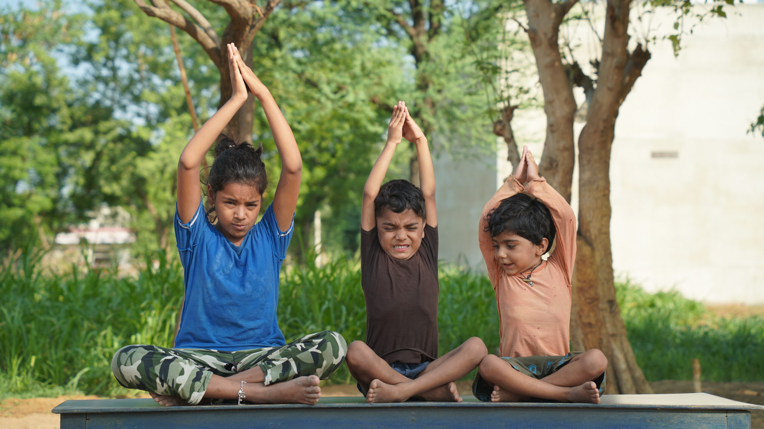 Children in blue and orange uniform participating in yoga practice in an open area.