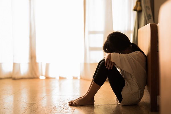 Image of a sad looking child sitting alone in a corridor, covering his face between his knees.