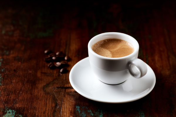 Image of a cup of coffee and some coffee beans kept on a wooden table.