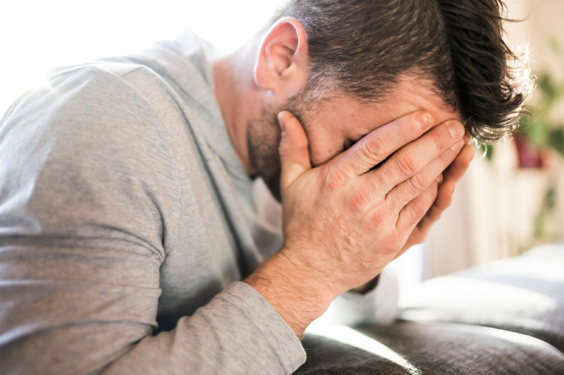 Close up image of a man sitting on a sofa with his hands covering his face in a sad and depressed condition.