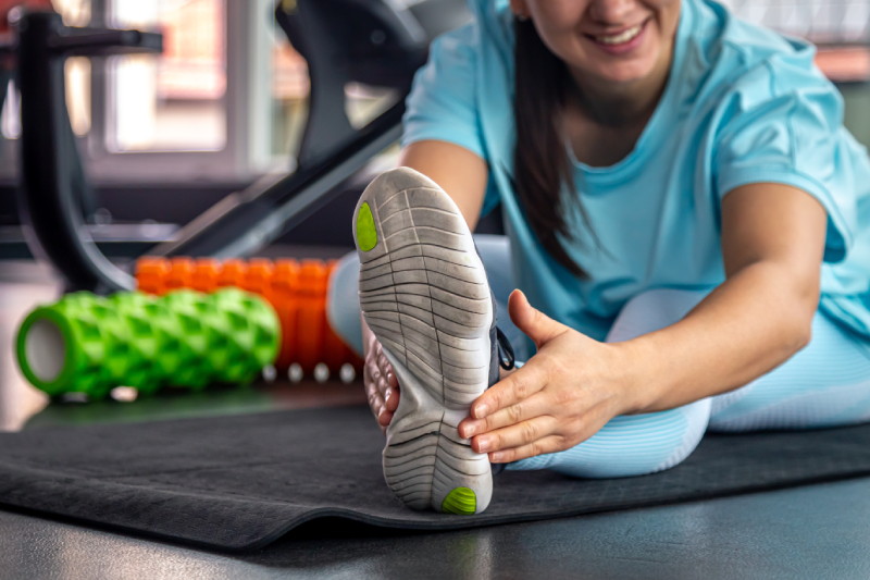 A woman sitting on a mat touches her feet doing a stretching exercise before training at gym.