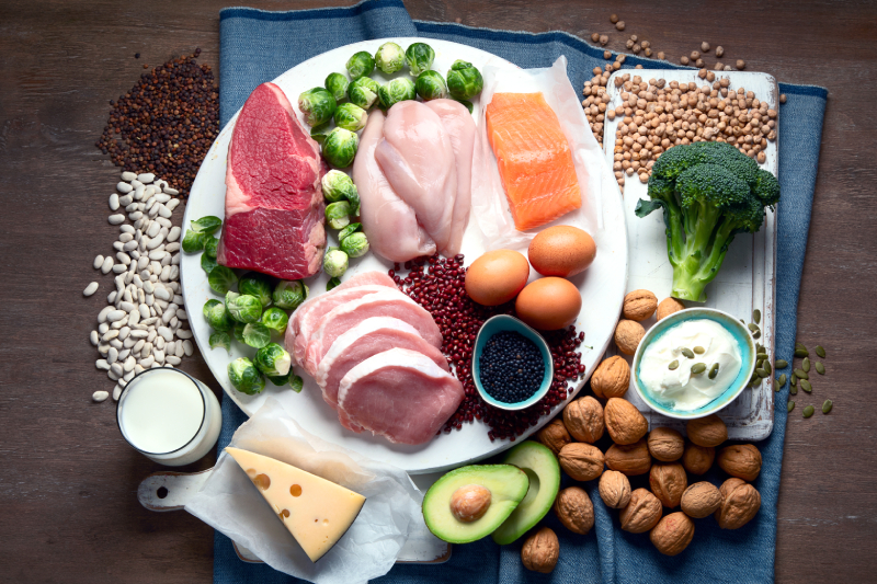 Top view of of different high protein foods kept in a plate and few spread on a blue cloth spread on a wooden table.