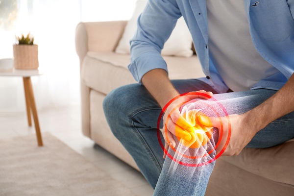 Close up view of a man sitting on a couch holding his knee in pain.