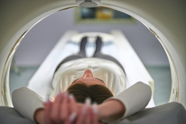 Close up view of a CT scanner with a young woman lying on the CT table with outstretched hands, undergoing a scan.