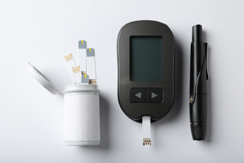 Top view of digital glucometer, lancet pen and test strips kept on a white background.