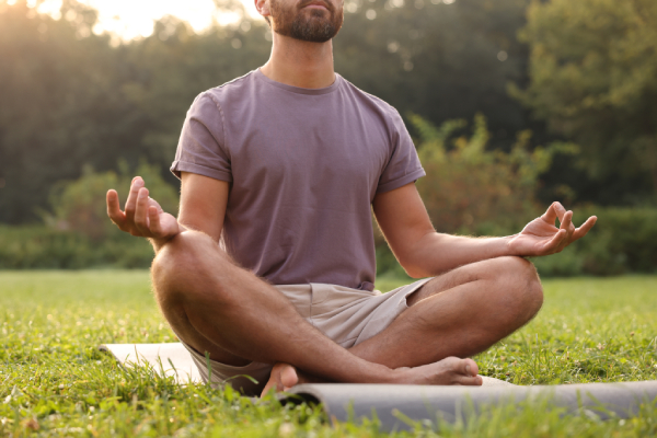 Image of a young man sitting outdoors on a mat with his hands kept stretched on his knees,doing yoga/meditation.