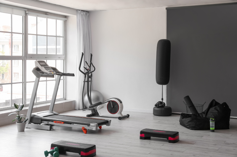 Interior view of a modern gym with a wide window, containing treadmill and other sport equipments.