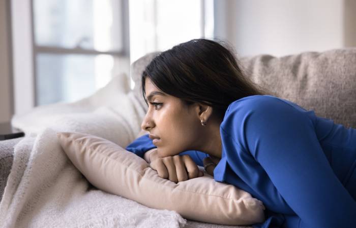 A depressed/sad looking young woman lying on the couch inside a living room.