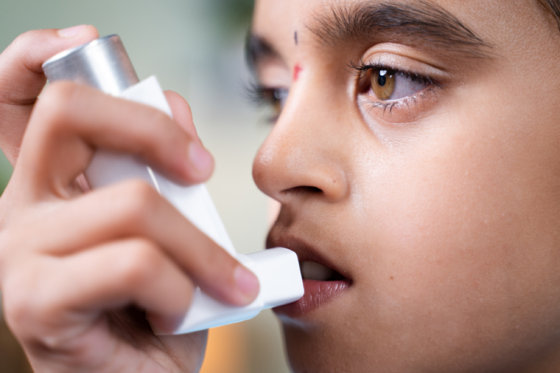 A close up image of a girl/child using an asthma medication inhaler.