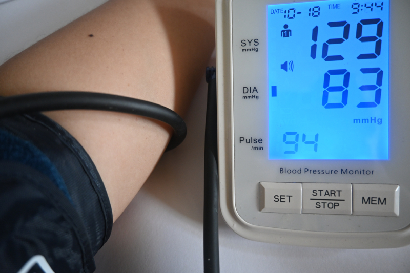 Close up image of a persons hand with a digital BP cuff connected to it and the monitor showing systolic and diastolic pressure readings.