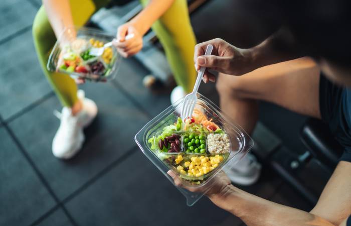 Top view of a young couple in workout costume, having healthy salad in a gym.