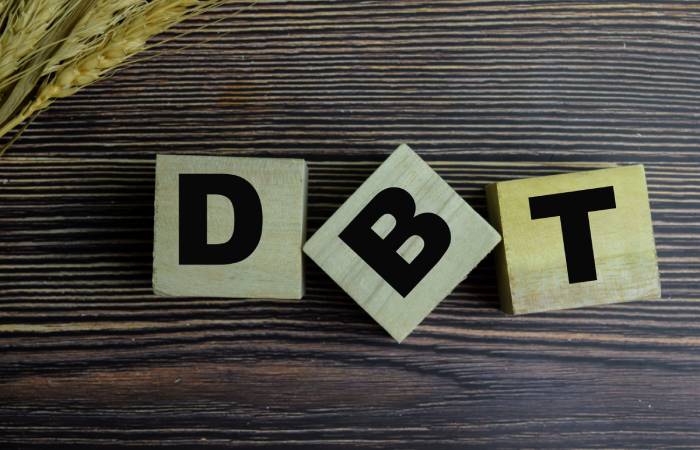 The letters DBT written on blocks displayed over a dark wooden background.