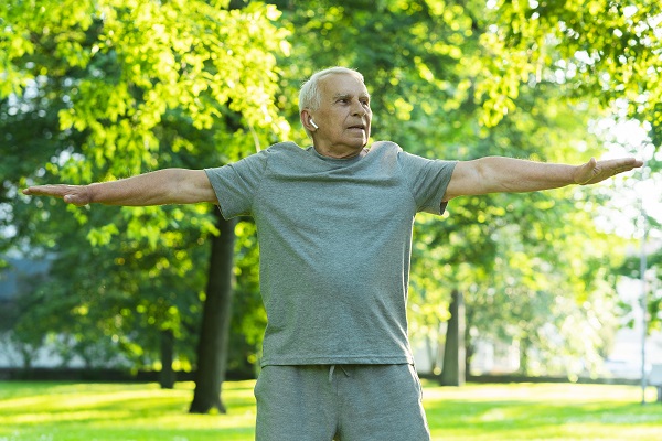 An active elderly man doing exercise in a park filled with trees and greenery around.