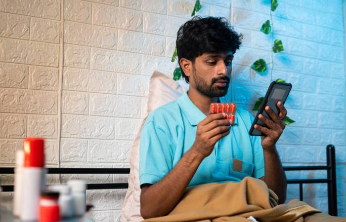 A man sitting on a bed orders medicines online using his mobile.