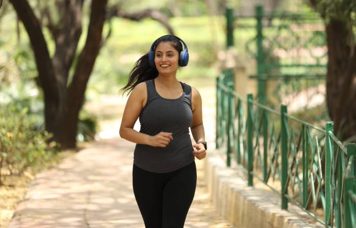 A happy young woman doing jogging in a park wearing headphones.