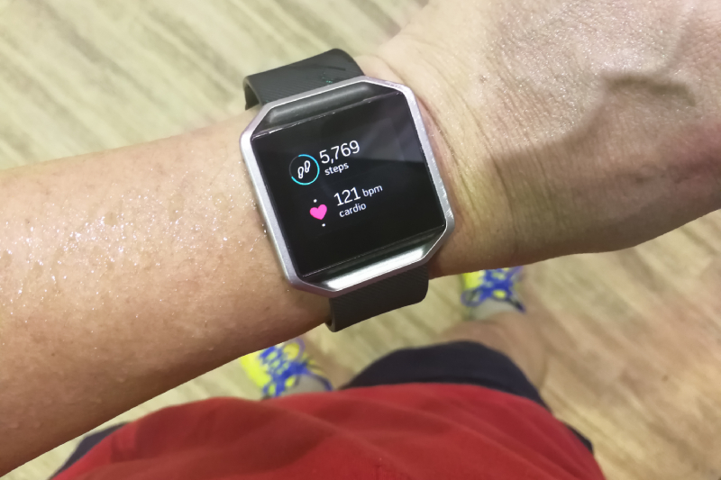 Top view of a man in workout costume looking at his smartwatch displaying the cardiac readings on a fitness app.