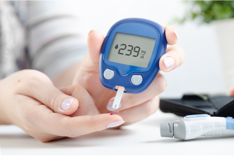 Close up image of a woman holding a glucometer in one hand , checking her blood sugar level from the other hand.