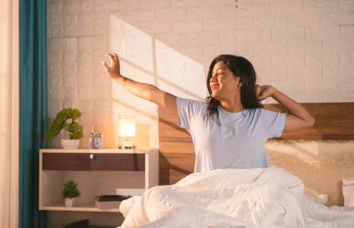 A happy woman wakes up in her bedroom in the morning, stretching her hands to start the day.