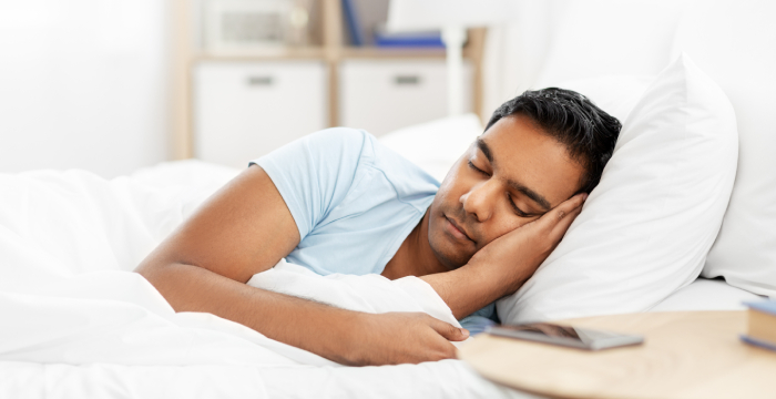 Front view of a man,lying on his left side sleeping peacefully in his white themed bedroom