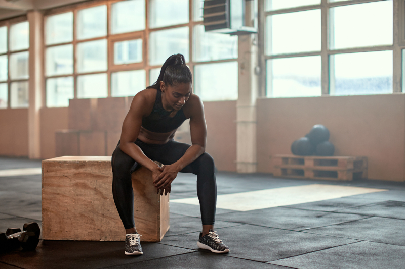 A healthy woman in sportswear sitting on a wooden box, taking a break after a box jump workout at the gym.