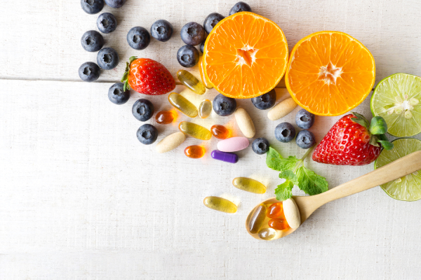 Multivitamin tablets and supplements along with fresh citrus fruits,blueberries and strawberries kept on a white wooden background.