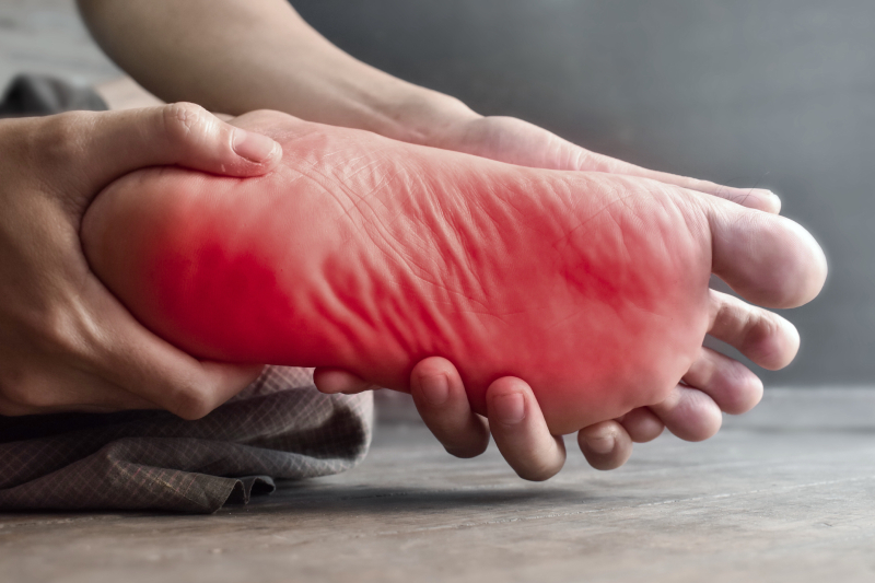 A person sitting on the floor presents a view of their foot from underneath, with a red shade.