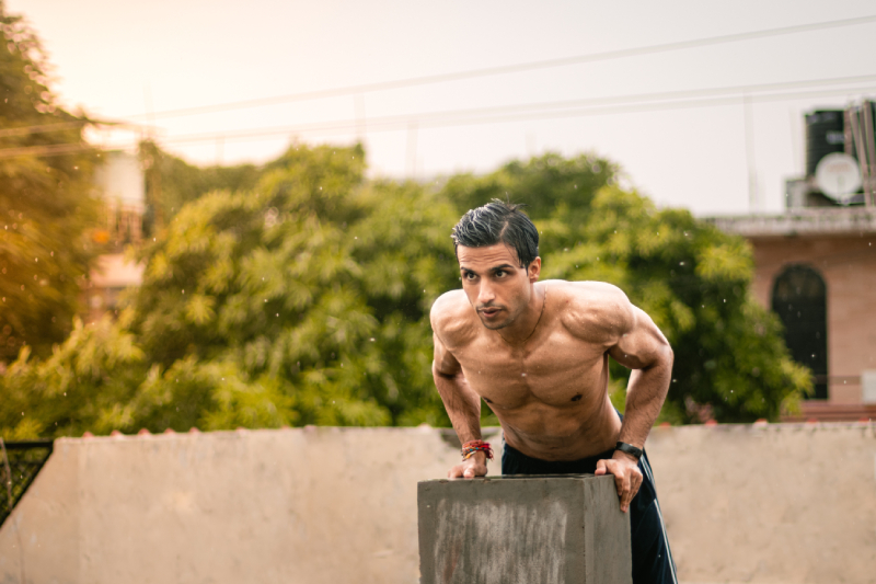 Image of an active healthy man doing muscle hypertrophy workout with the support of a short pillar on the terrace of a building.