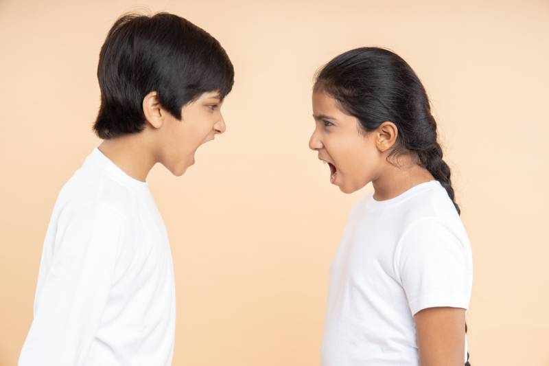 An angry boy and a girl standing before a beige background, shouts at each other.