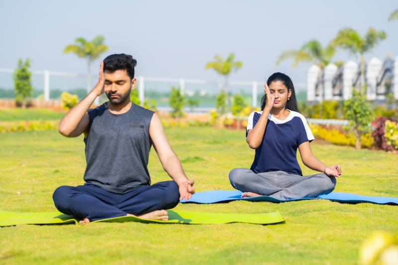 A young couple doing pranayama sitting in a park.