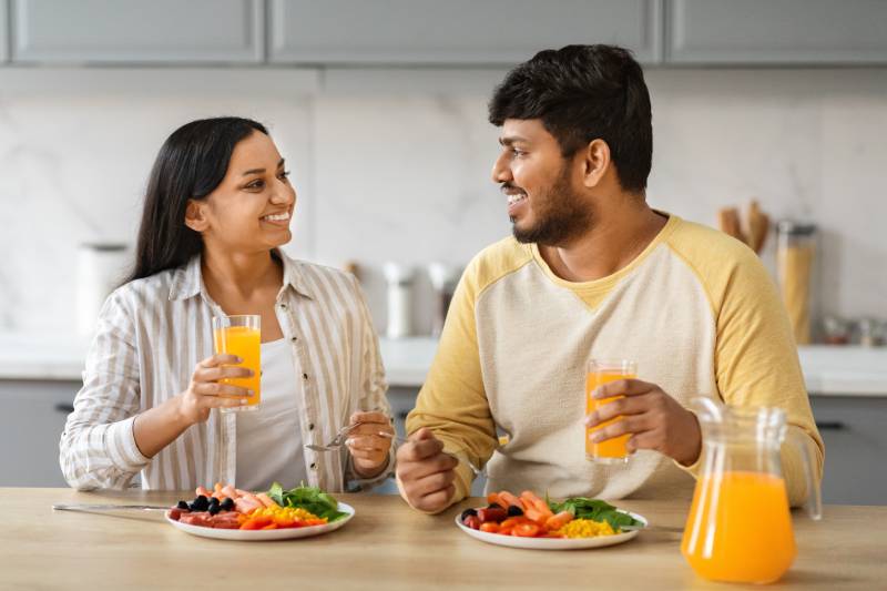 A young couple having a happy conversation while enjoying healthy food at home.