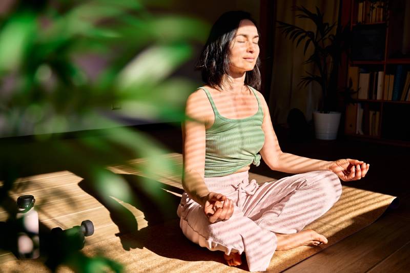 A woman doing meditation sitting on a yoga mat at home.